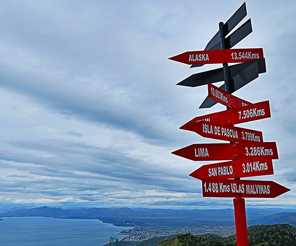 A road sign lists place locations from Alaska to the southernmost point in Argentina and the distances from the sign.
