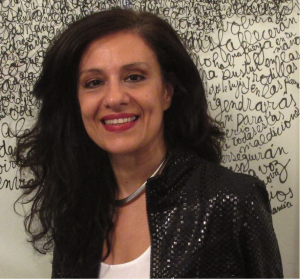Andrea Giunta is smiling in a shiny black jacket, white t-shirt, and silver collar.