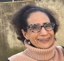 Gabriela Cano is smiling in a light-pink sweater, gray earrings, glasses, and a tiara.