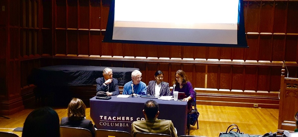 panel of four seated at a table with a dropdown screen in the background during conference at Teachers College 