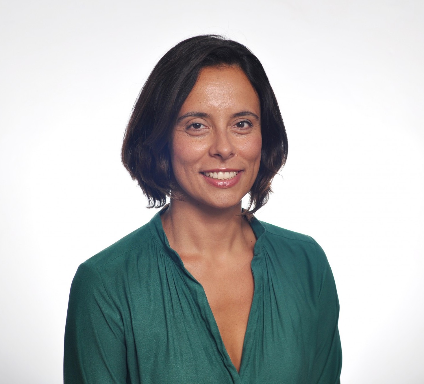Joana is smiling against a white background. She has dark brown hair and is wearing a green shirt.