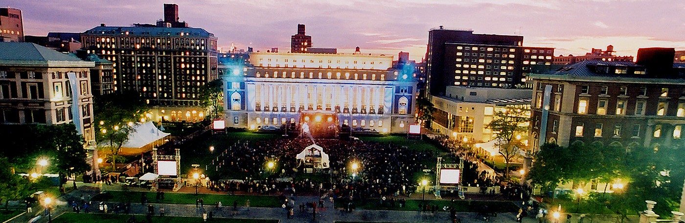 Aerial photograph of Columbia University's Morningside campus at dusk, building lights twinkle against a blueish-purple sky