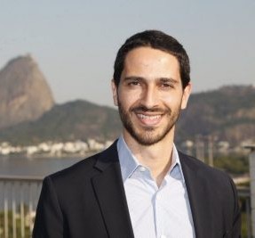 Ronaldo Lemos is smiling in a black blazer and light-blue shirt. Rio de Janeiro's Sugarloaf Mountain is in the background.