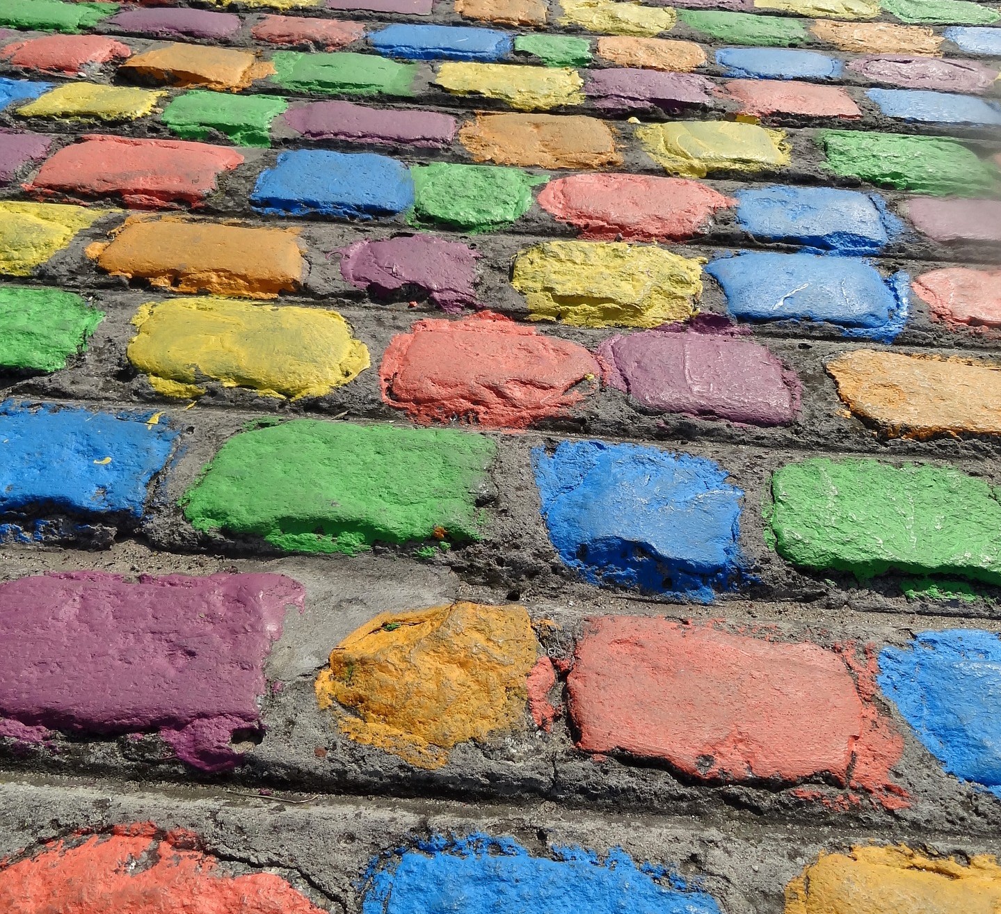 The picture shows a cobbled stone wall with painted stones in multiple different colors.