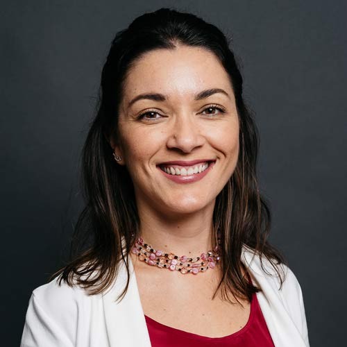 Ilona Szabo is smiling in a white jacket, burgundy shirt, and pink collar.