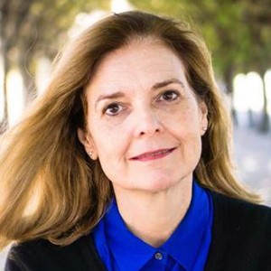 A woman wearing a bright blue blouse smiles into the camera beneath a tree.