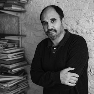 Pablo Pineau stands in jeans and a dark sweater next to bookshelves overflowing with books and journals.