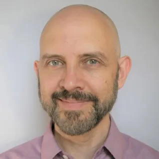 A man, Paulo Blikstein, wearing a pink button up shirt smiles into the camera.