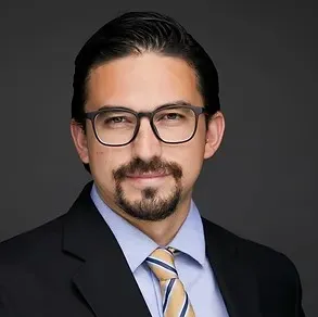 Jorge is wearing a black blazer with a blue shirt underneath. 
