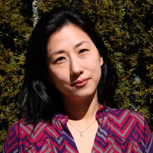 A woman with dark shoulder-length hair and wearing a brightly colored blouse smiles slightly into the camera.